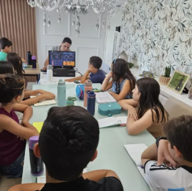Turma de crianças em aula presencial acompanhando gráficos na tela